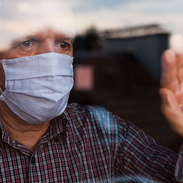 man touching window and looking out wearing a mask man touching window and looking out wearing a mask