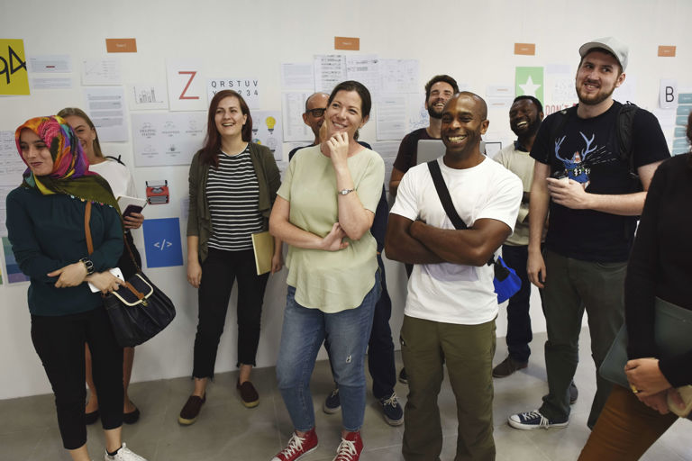 Group of people standing and smiling whilst listening to someone talk Group of people standing and smiling whilst listening to someone talk