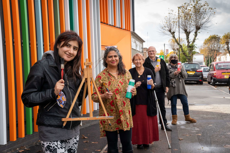 people standing outside a colourful building holding art supplies people standing outside a colourful building holding art supplies