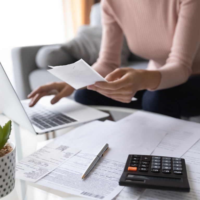 lady sitting on couch looking at a piece of paper and typing on her laptop lady sitting on couch looking at a piece of paper and typing on her laptop