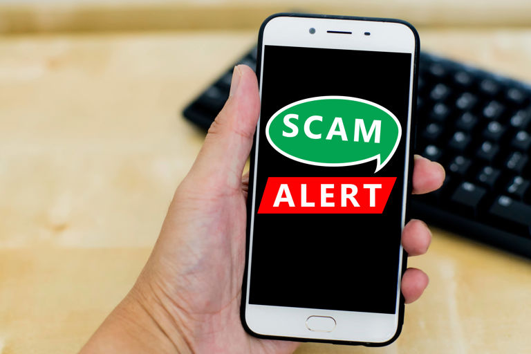 hand holding a white mobile phone with a scam alert warning hand holding a white mobile phone with a scam alert warning