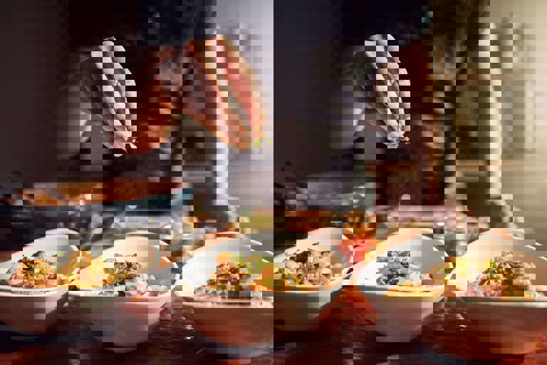 Hand drizzling herbs on food in a bowl Hand drizzling herbs on food in a bowl