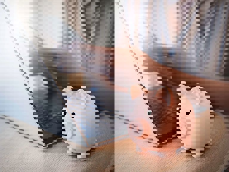 women on laptop and mobile phone with a pink piggy bank on the table women on laptop and mobile phone with a pink piggy bank on the table