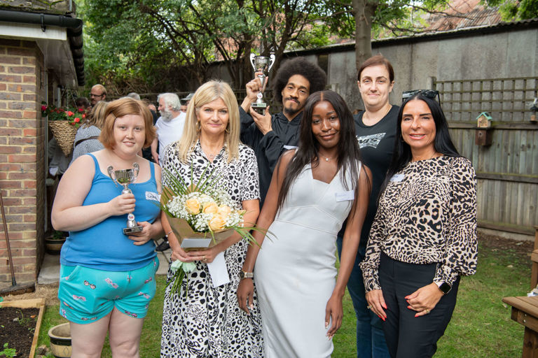 six people standing in a garden in a housing scheme holding a trophy and flowers six people standing in a garden in a housing scheme holding a trophy and flowers