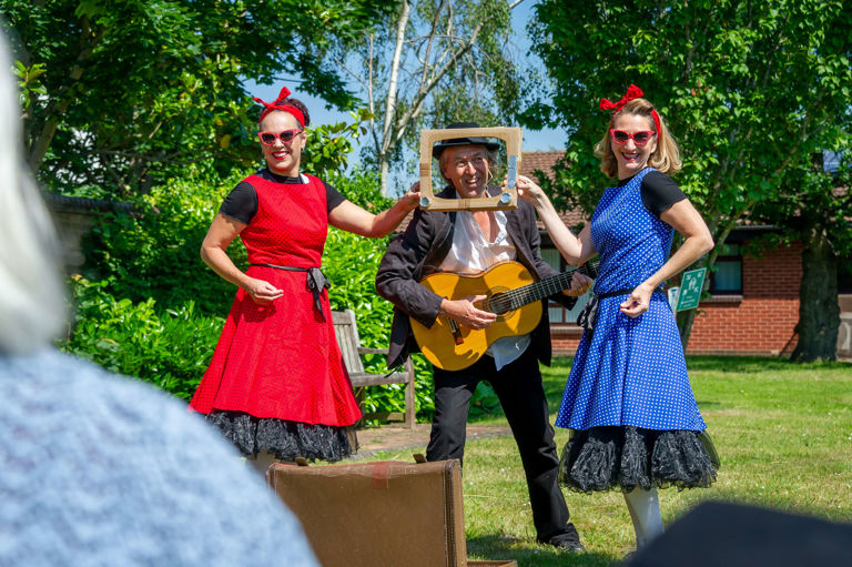 two ladies in dresses standing next to a man playing the guitar two ladies in dresses standing next to a man playing the guitar