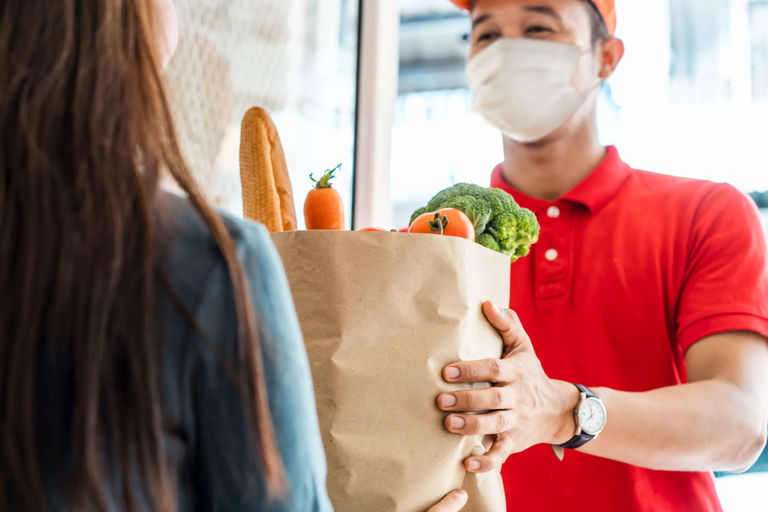 Asian man wearing a mask and delivering groceries to a lady at the door Asian man wearing a mask and delivering groceries to a lady at the door