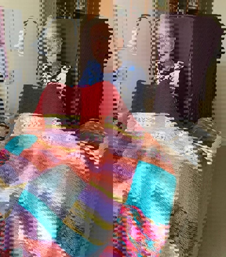 Elderly lady sitting under a colourful blanket Elderly lady sitting under a colourful blanket