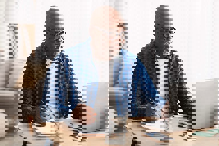 image of man in a blue shirt using a laptop and writing on a notepad image of man in a blue shirt using a laptop and writing on a notepad