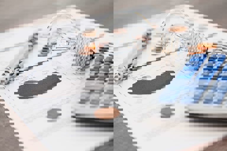 lightbulb coin calculator with blue buttons and a silver pen lying on a document on a table lightbulb coin calculator with blue buttons and a silver pen lying on a document on a table