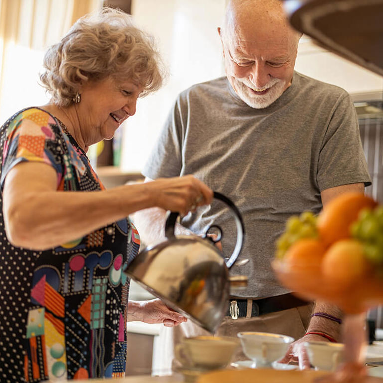 elderly woman pouring water from a kettle in the cup with a elderly man elderly woman pouring water from a kettle in the cup with a elderly man