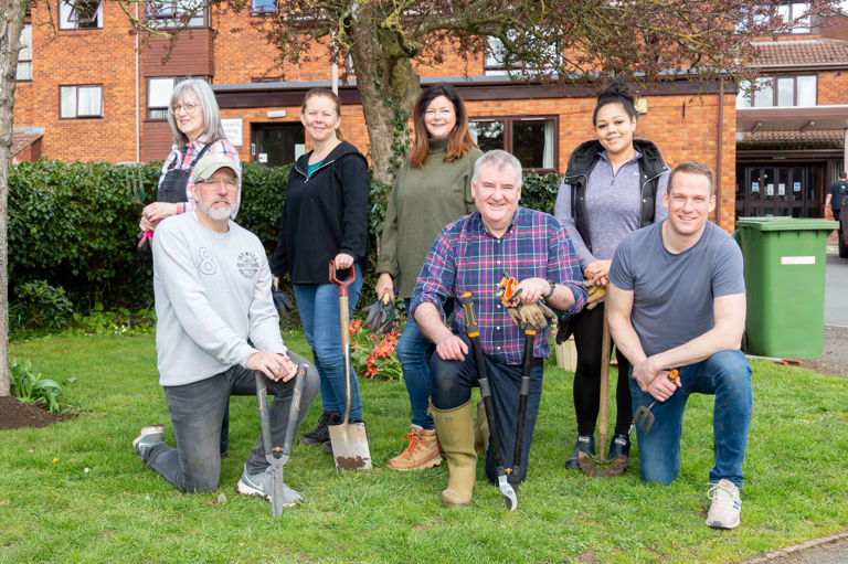 seven people on a green lawn smiling holding garden tools seven people on a green lawn smiling holding garden tools