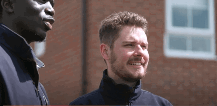 two men standing in front of a brick building two men standing in front of a brick building
