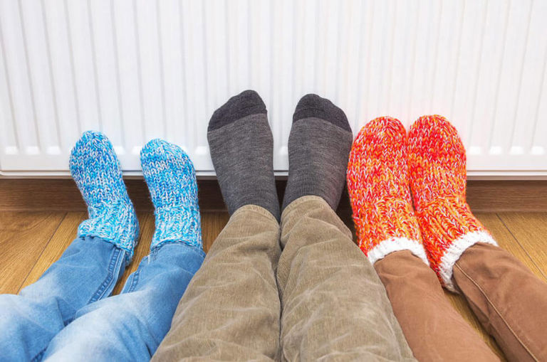 three sets of feet in socks in front of a heater three sets of feet in socks in front of a heater